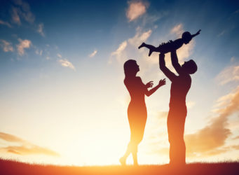 Happy family together, parents with their little child at sunset. Father raising baby up in the air.