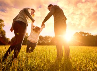 Photo of a couple holding their child's hands with sun setting in background